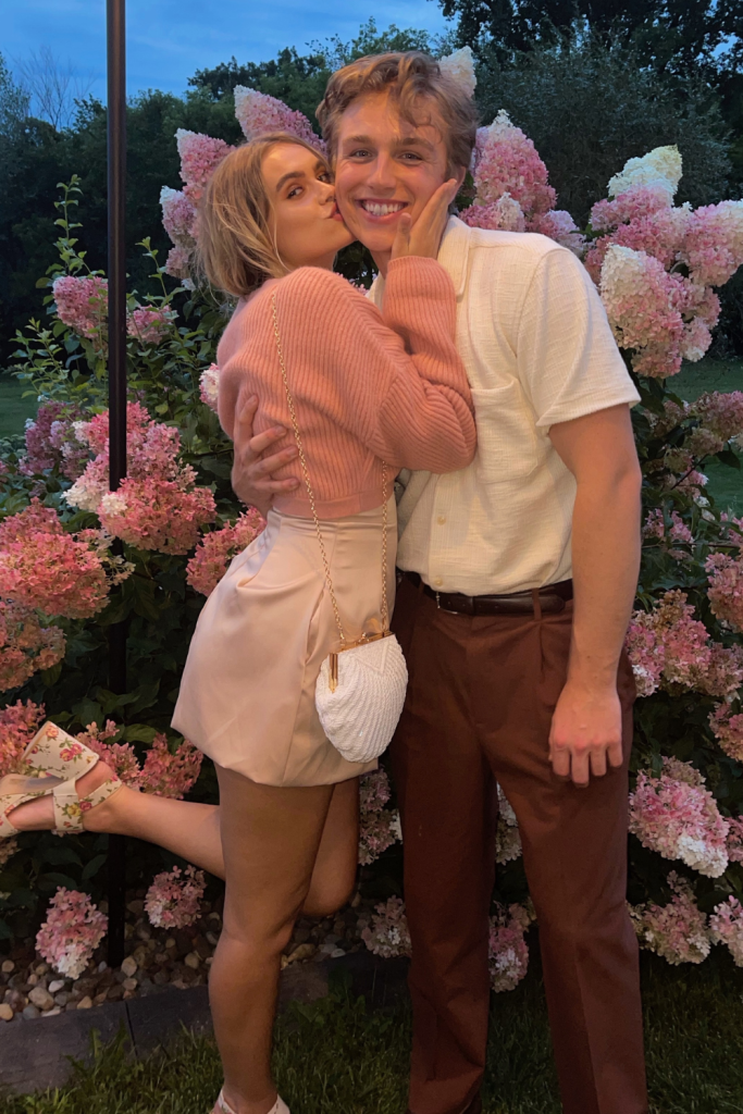 a man and woman kissing in front of a bush of flowers